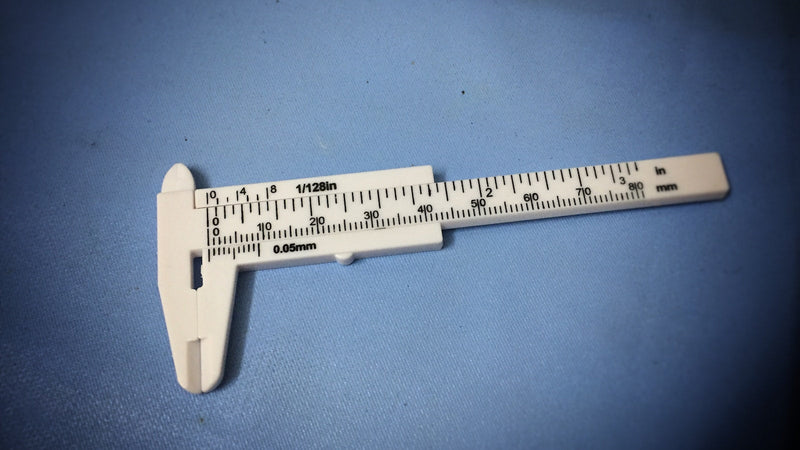 White vernier caliper on a blue surface. Photo by Ag PIC on Unsplash.