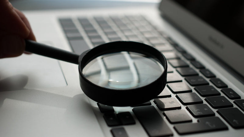 Magnifying glass held over a laptop keyboard. Photo by Agence Olloweb on Unsplash.
