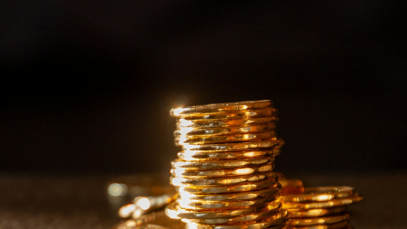 Stacks of gold coins on a dark surface. Photo by Anthony Aird on Unsplash.