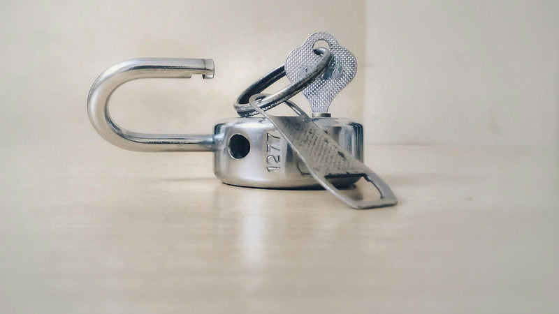 Open padlock with a key on a light surface. Photo by Basil James on Unsplash.