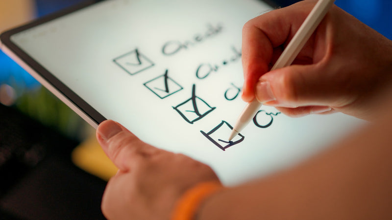 A hand ticks items off a checklist on a tablet. Photo by Jakub Zerdzicki on Unsplash.