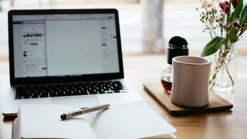 Laptop, open notebook and coffee on a desk. Photo by Nick Morrison on Unsplash.