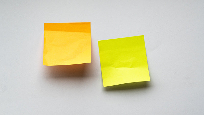 Two sticky notes, one orange and one yellow, on a white surface. Photo by Paper Textures on Unsplash.